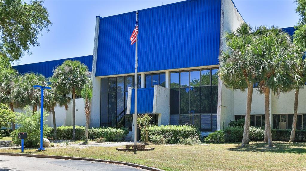 A two-story commercial building features a blue metal facade, large glass windows, and palm trees — 2 COMMERCE BOULEVARD, PALM COAST, FL