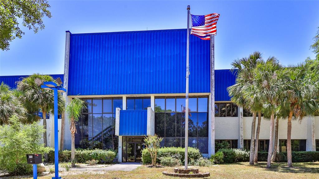 A two-story commercial building with blue metal siding, glass windows, and an American flag — 2 COMMERCE BOULEVARD, PALM COAST, FL