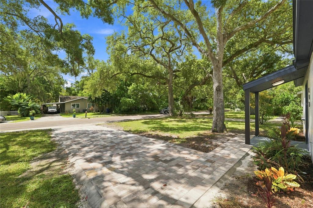 A paved walkway leads to a covered entrance under large trees in a residential yard — 510 3RD AVENUE NE, LARGO, FL