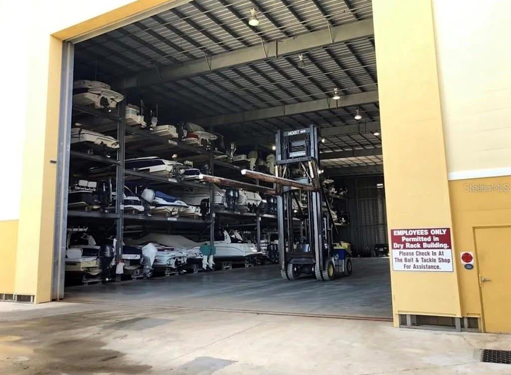 A large open-air warehouse features multi-level metal racks storing numerous boats and a forklift — 570 BLACKBURN POINT ROAD UNIT 11, OSPREY, FL