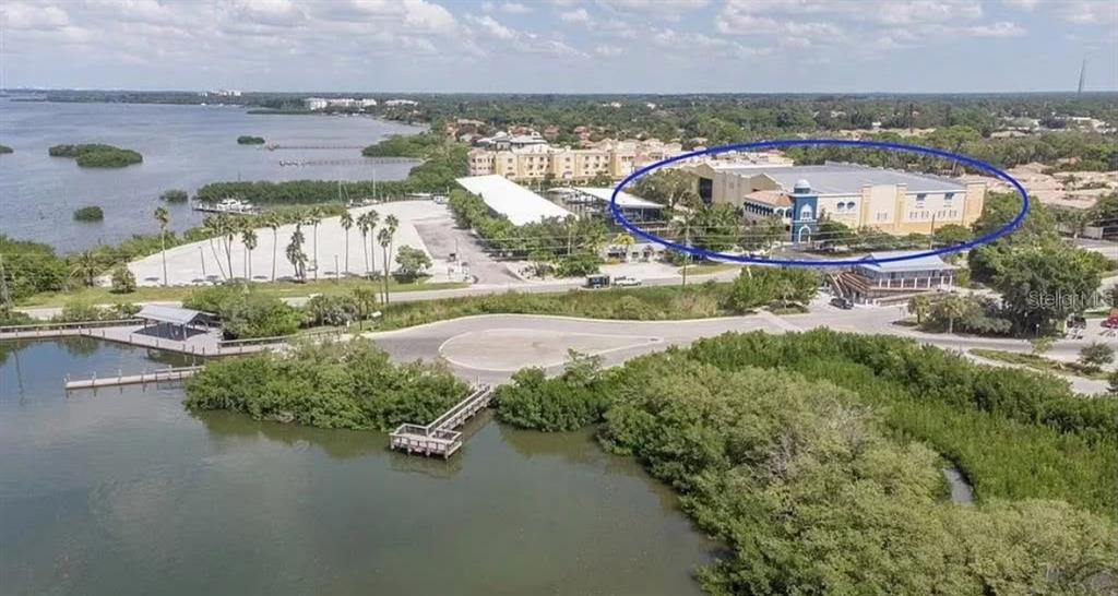 An aerial view shows a large building complex near a waterfront with docks and vegetation — 570 BLACKBURN POINT ROAD UNIT 11, OSPREY, FL