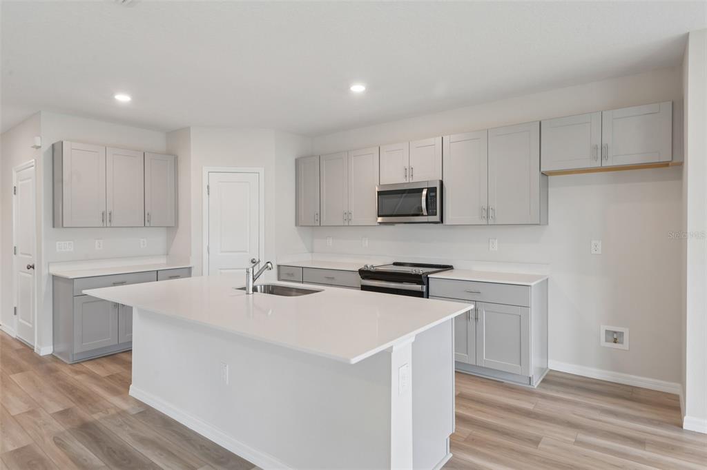A kitchen features gray cabinets, white countertops, a central island, and light wood-look flooring — 35033 ARBOR RETREAT DRIVE, DADE CITY, FL