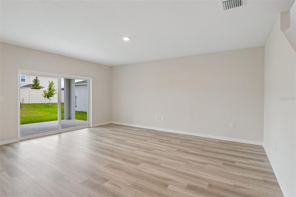 An empty room with light wood-look flooring, beige walls, and a sliding glass door — 35033 ARBOR RETREAT DRIVE, DADE CITY, FL