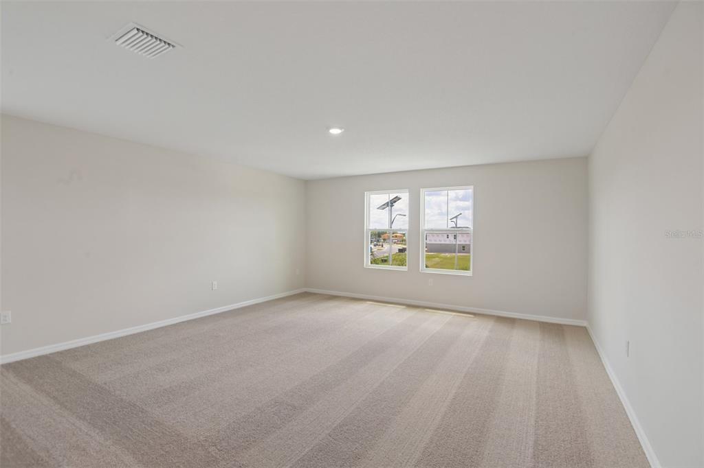 An empty room with beige carpet, light-colored walls, and two windows overlooking a construction site — 35033 ARBOR RETREAT DRIVE, DADE CITY, FL