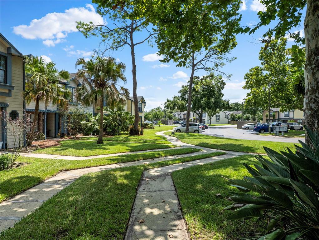 A sidewalk winds through a grassy courtyard between apartment buildings and a parking lot — 2820 REVERE COURT, CASSELBERRY, FL