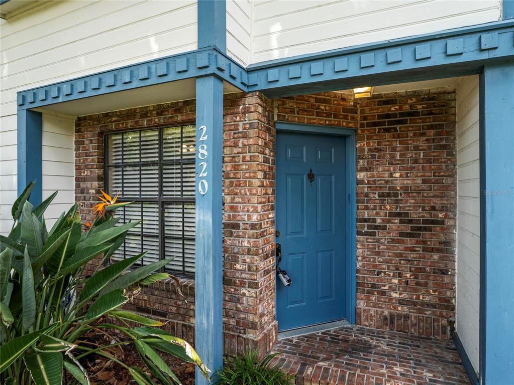 A blue front door is set into a brick wall next to a window with shutters — 2820 REVERE COURT, CASSELBERRY, FL