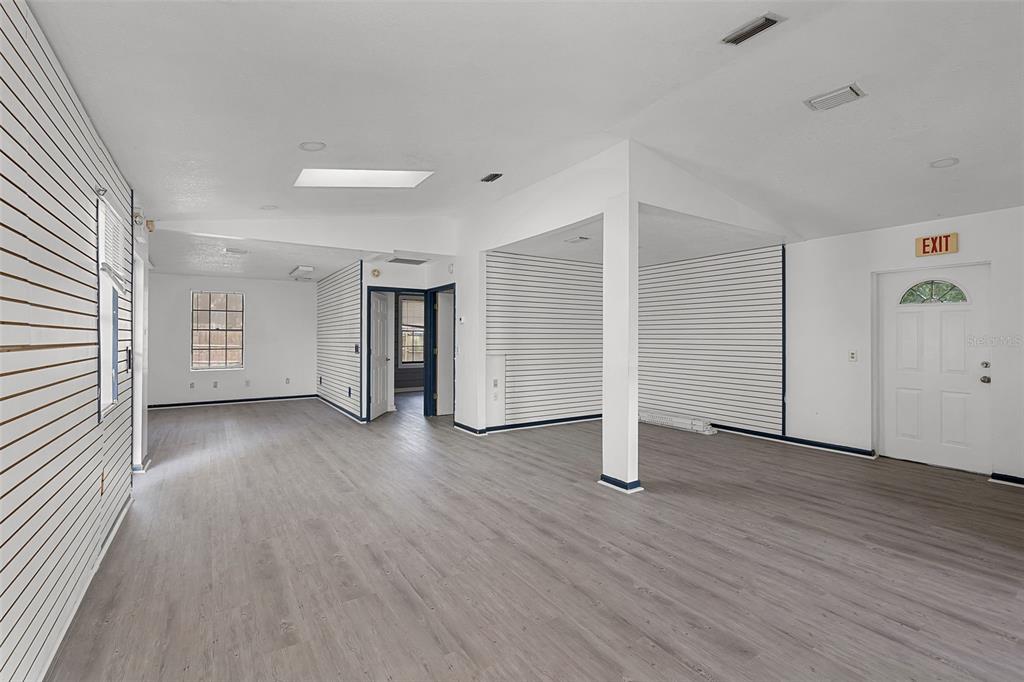 An interior view of a commercial space with white slat walls, gray flooring, and an exit — 697 E ANDERSON ROAD, GROVELAND, FL