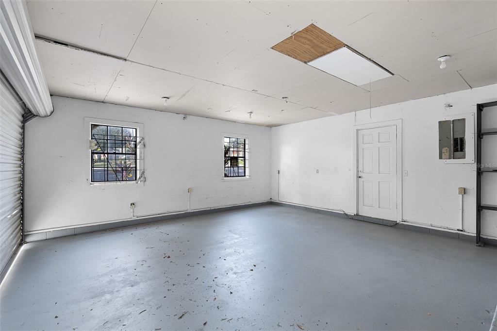 An empty garage with white walls, a gray floor, two windows, and a ceiling access panel — 697 E ANDERSON ROAD, GROVELAND, FL