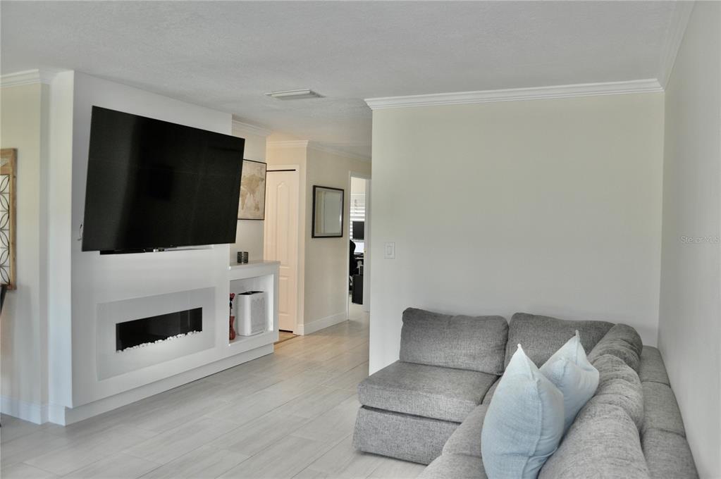 A living room features a wall-mounted television above a fireplace, light flooring, and a sofa — 150 POOLE PLACE, OLDSMAR, FL
