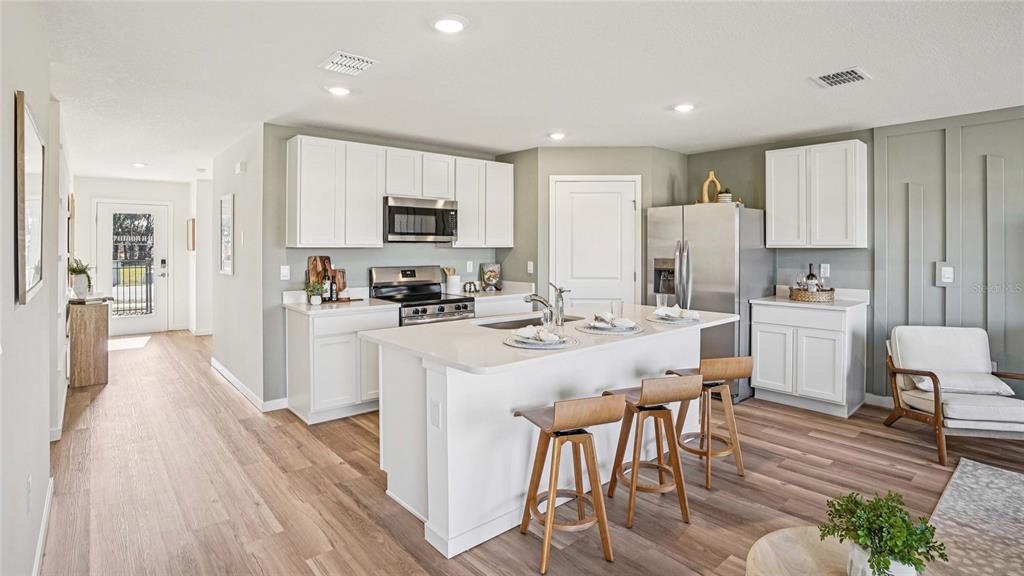 A modern kitchen features white cabinetry, a central island with bar stools, and wood flooring — 4584 KONA CIRCLE, SPRING HILL, FL