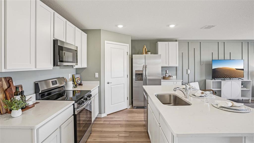 A modern kitchen features white cabinets, stainless steel appliances, a center island, and wood flooring — 4584 KONA CIRCLE, SPRING HILL, FL