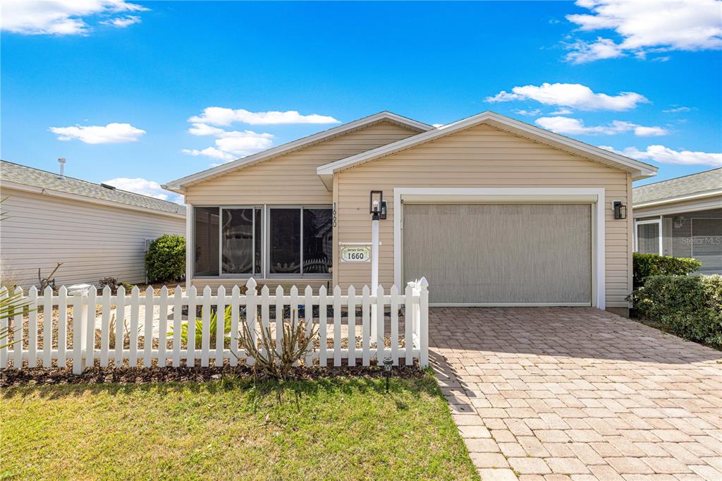 A single-story house with tan siding, a white picket fence, and a paved driveway — 1660 ORR TERRACE, THE VILLAGES, FL