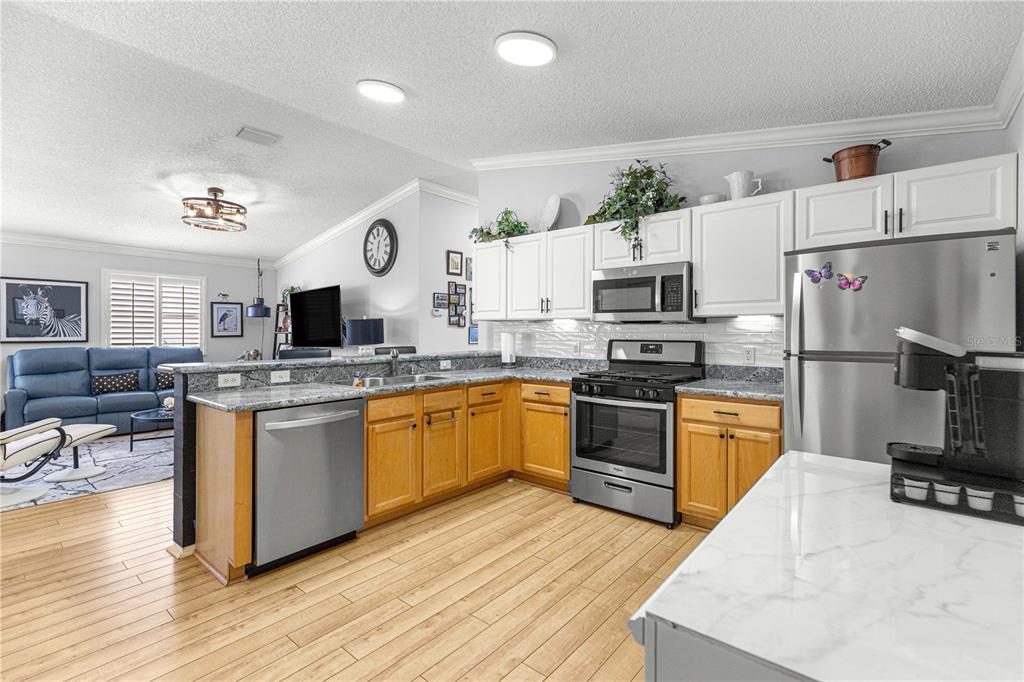 A kitchen with wood cabinets and granite countertops opens to a living area with flooring — 1660 ORR TERRACE, THE VILLAGES, FL