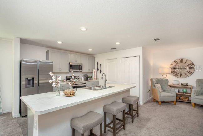 A kitchen features a white island with bar stools, gray cabinets, and stainless steel appliances — 947 SALERNO COURT, KISSIMMEE, FL