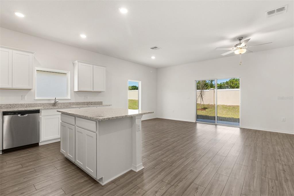 A kitchen with a granite-topped island and stainless steel dishwasher opens to a living area — 1798 WHITE ELEPHANT LOOP, WINTER HAVEN, FL