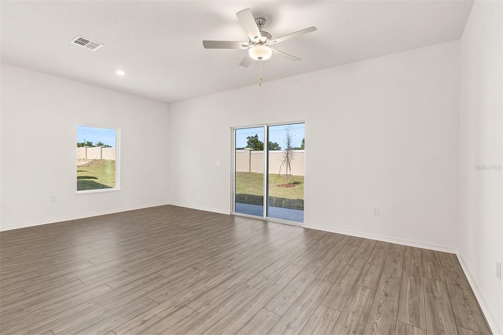 An empty room with white walls, wood-look flooring, a ceiling fan, and sliding glass doors — 1798 WHITE ELEPHANT LOOP, WINTER HAVEN, FL