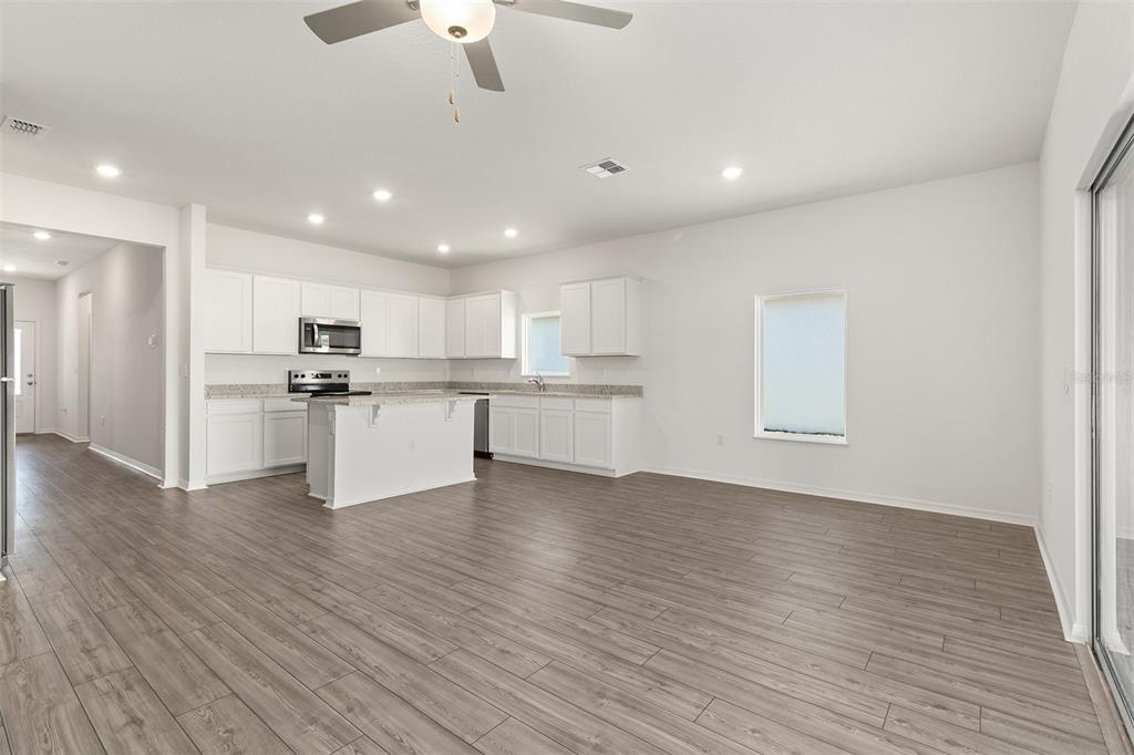 A kitchen with white cabinets, an island, and wood-look flooring opens into a living area — 1798 WHITE ELEPHANT LOOP, WINTER HAVEN, FL