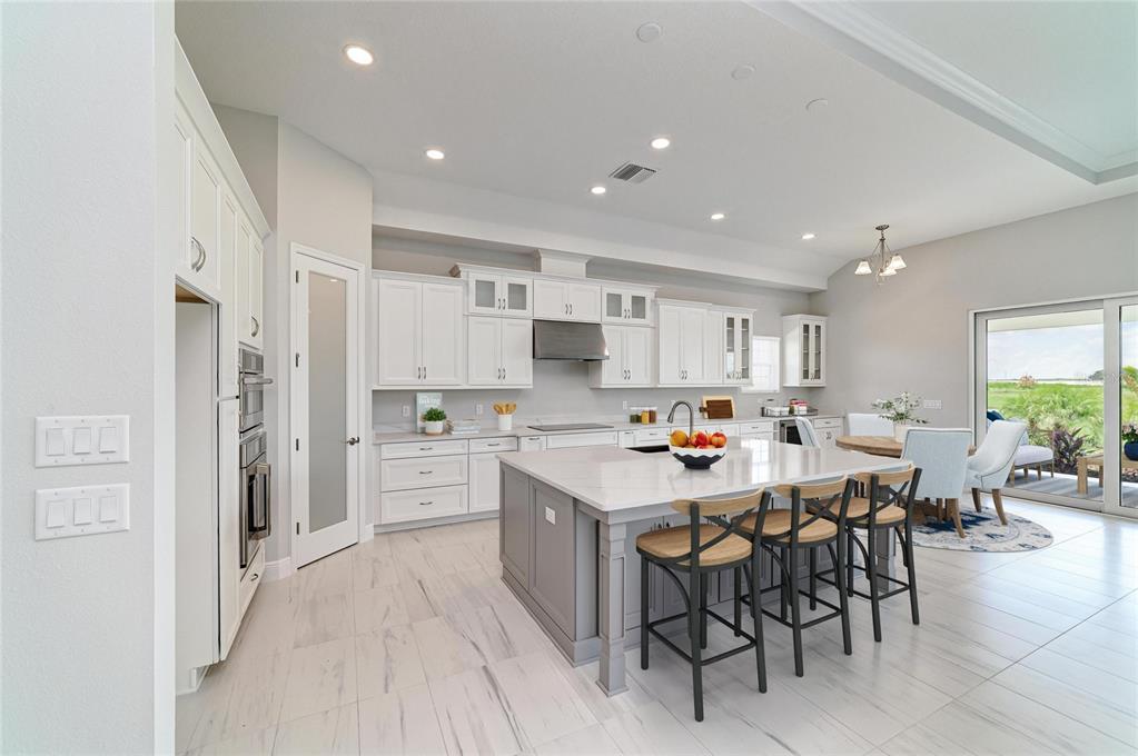 A modern kitchen features white cabinetry, a gray island with bar seating, and tile flooring — 10183 LILAC MANOR TRACE, SAN ANTONIO, FL