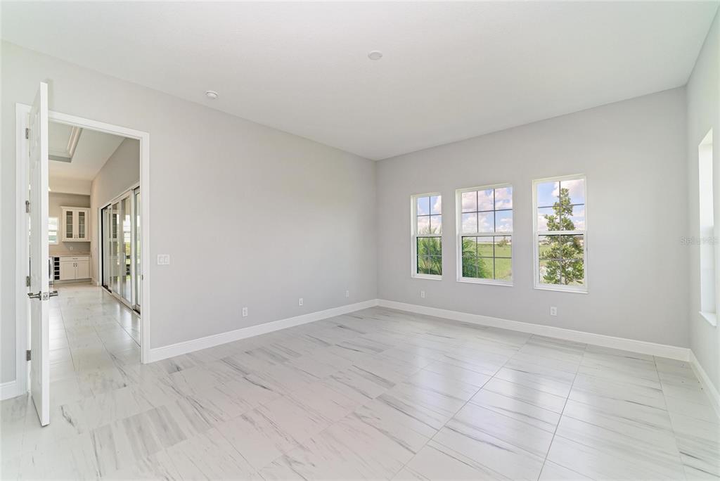 An empty room with light gray walls, white tile flooring, and three windows overlooking greenery — 10183 LILAC MANOR TRACE, SAN ANTONIO, FL