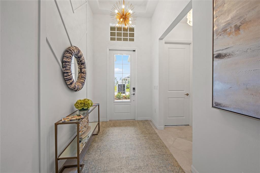 A bright entryway features a gold chandelier, a console table, and a white front door — 7161 INLET ISLES COURT, LAKEWOOD RANCH, FL