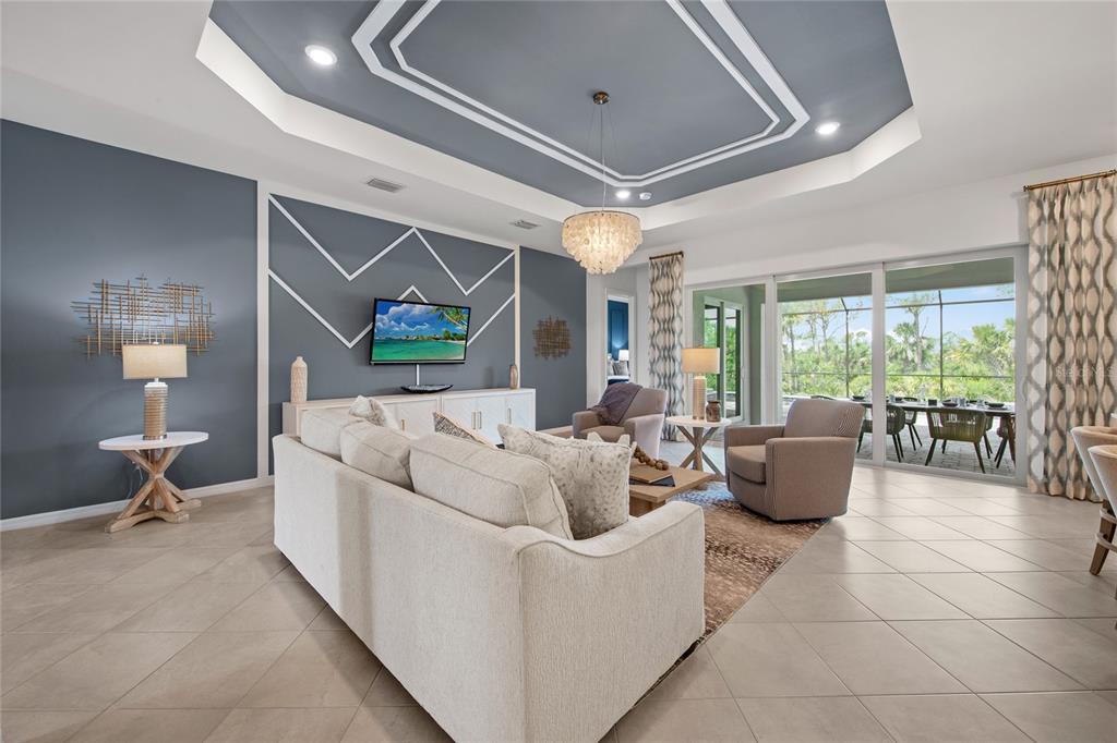 A living room features a tray ceiling, blue accent wall with geometric trim, and sliding doors — 7161 INLET ISLES COURT, LAKEWOOD RANCH, FL