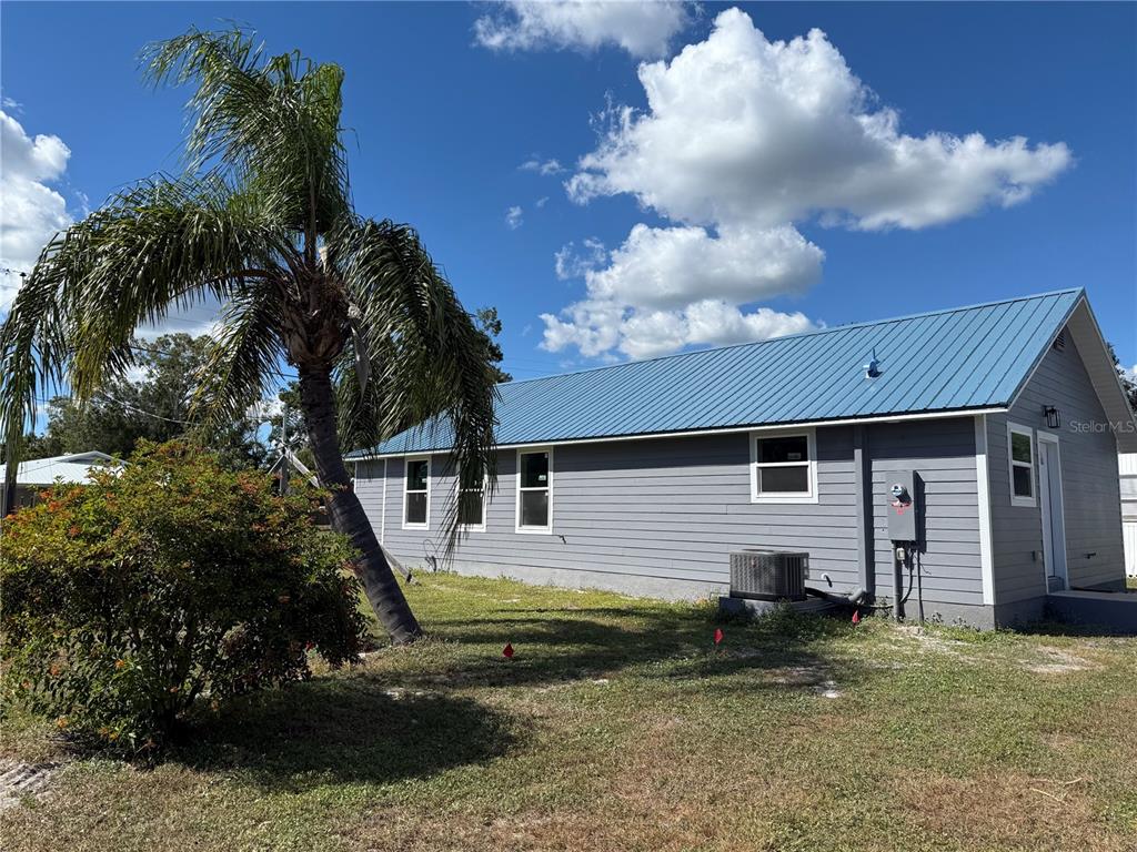 A gray house with a blue metal roof stands next to a palm tree — 103 S ROGERS AVENUE, ARCADIA, FL