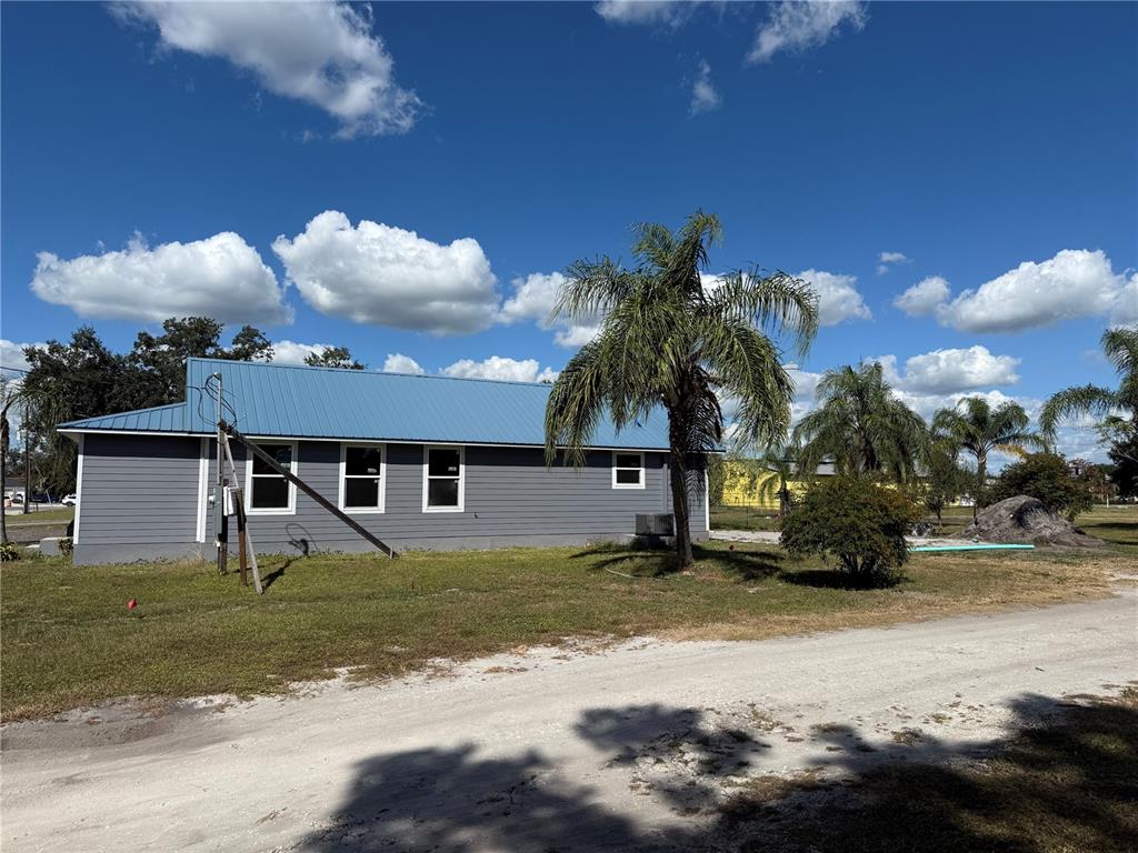 A gray house with a blue metal roof sits on a grassy lot with palms — 103 S ROGERS AVENUE, ARCADIA, FL