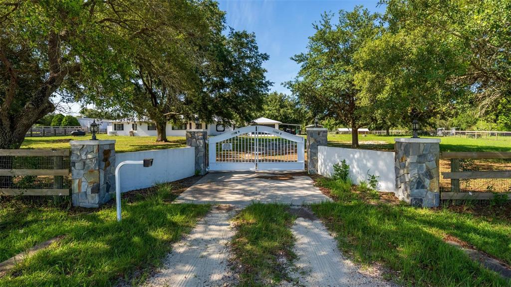 A white metal gate stands between two stone pillars at the entrance to a property — 12650 SE 98TH LANE, DUNNELLON, FL