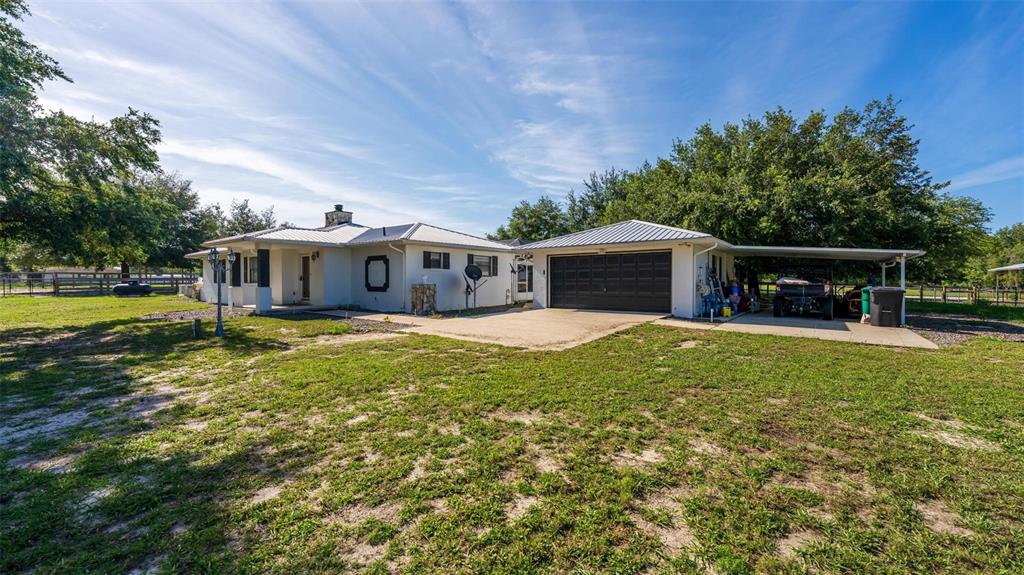 A white single-story house with a metal roof, attached garage, and a large grassy yard — 12650 SE 98TH LANE, DUNNELLON, FL