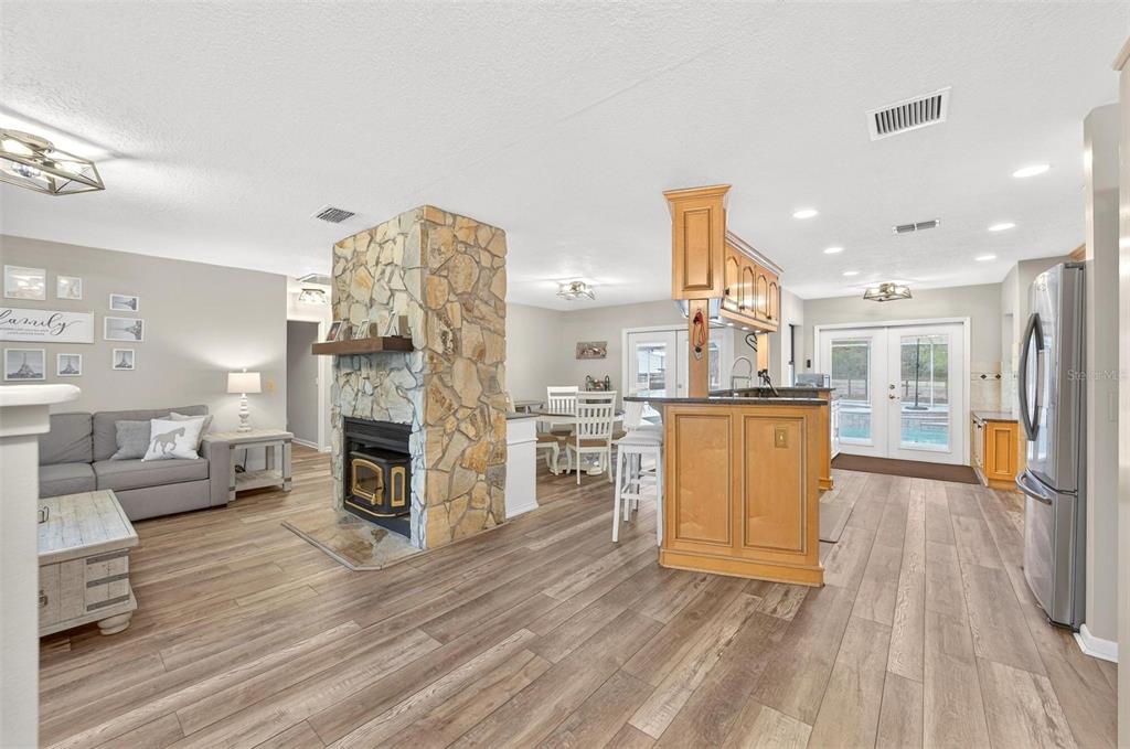 An open-concept living room and kitchen featuring a stone fireplace and wood-look flooring — 12650 SE 98TH LANE, DUNNELLON, FL