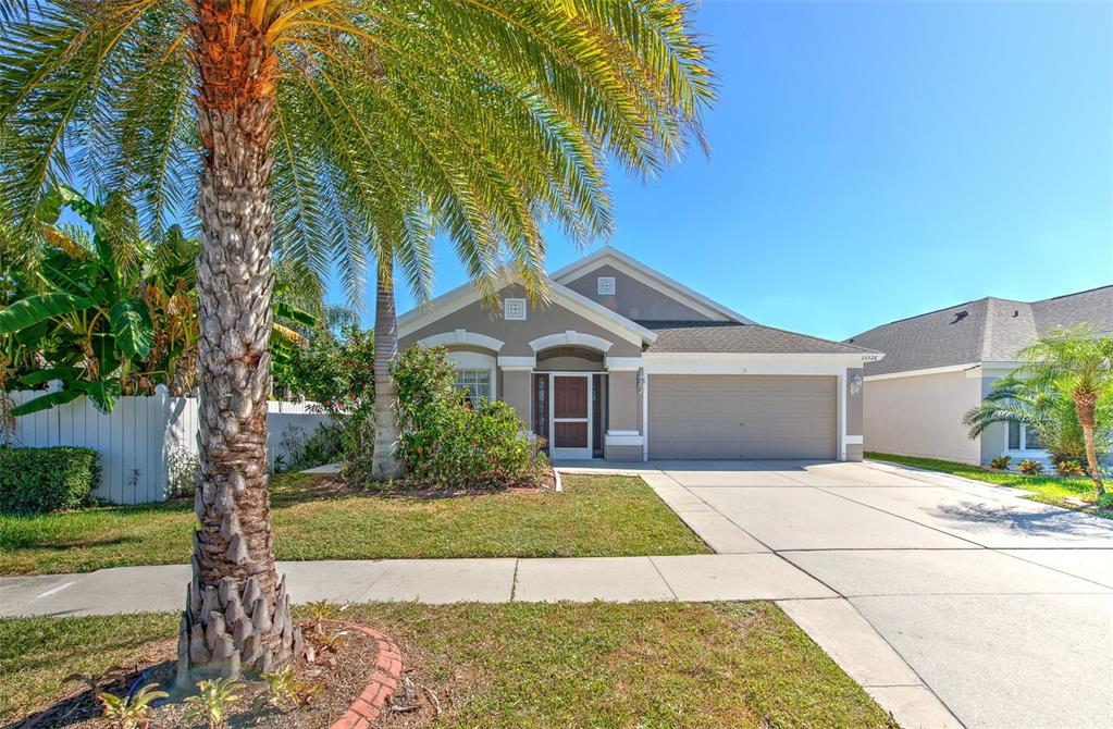 A single-story house with a beige stucco exterior, a two-car garage, and a palm tree — 13326 EVENING SUNSET LANE, RIVERVIEW, FL