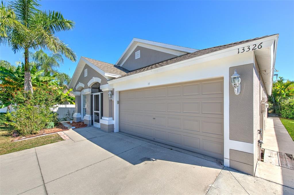 A single-story house exterior features a beige garage door, a front entryway, and palm trees — 13326 EVENING SUNSET LANE, RIVERVIEW, FL