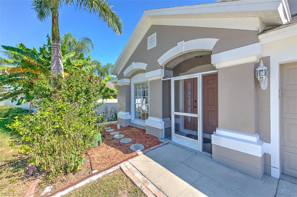 A tan house exterior features a screened front door, a palm tree, and landscaping — 13326 EVENING SUNSET LANE, RIVERVIEW, FL