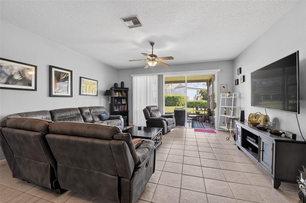 A living room features tile flooring, a large sectional sofa, a television, and sliding glass doors — 2823 CONCH HOLLOW DRIVE, BRANDON, FL