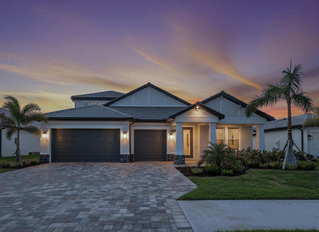 A single-story house with a three-car garage, stone accents, and a paver driveway at sunset — 1684 LUGANO CIRCLE, NOKOMIS, FL