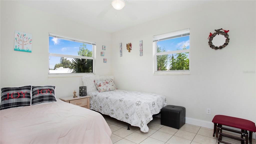 A bedroom features two twin beds, tiled flooring, and two windows with outdoor views — 515 YORK ROAD, LEHIGH ACRES, FL