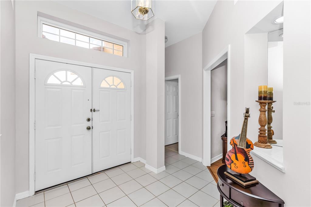 An entryway with white double doors, light-colored tile flooring, and a decorative violin-shaped tabletop ornament — 414 FAIRLANE DRIVE, DEBARY, FL