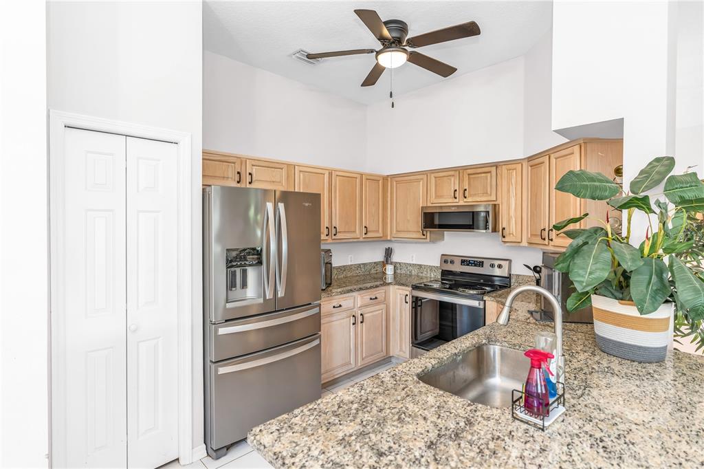 A kitchen features stainless steel appliances, light wood cabinets, granite countertops, and a ceiling fan — 414 FAIRLANE DRIVE, DEBARY, FL