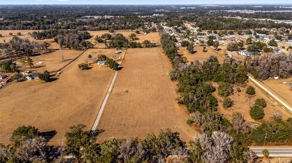 An aerial view shows a large, dry, rectangular field with a long driveway and trees — 4101 SE 110TH STREET, BELLEVIEW, FL