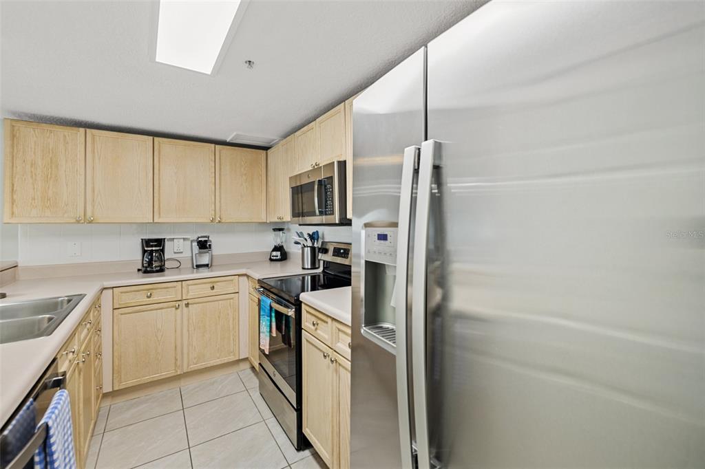 A kitchen features light wood cabinets, stainless steel appliances, and beige countertops over tiled floors — 5300 S ATLANTIC AVENUE UNIT 1-505, NEW SMYRNA BEACH, FL