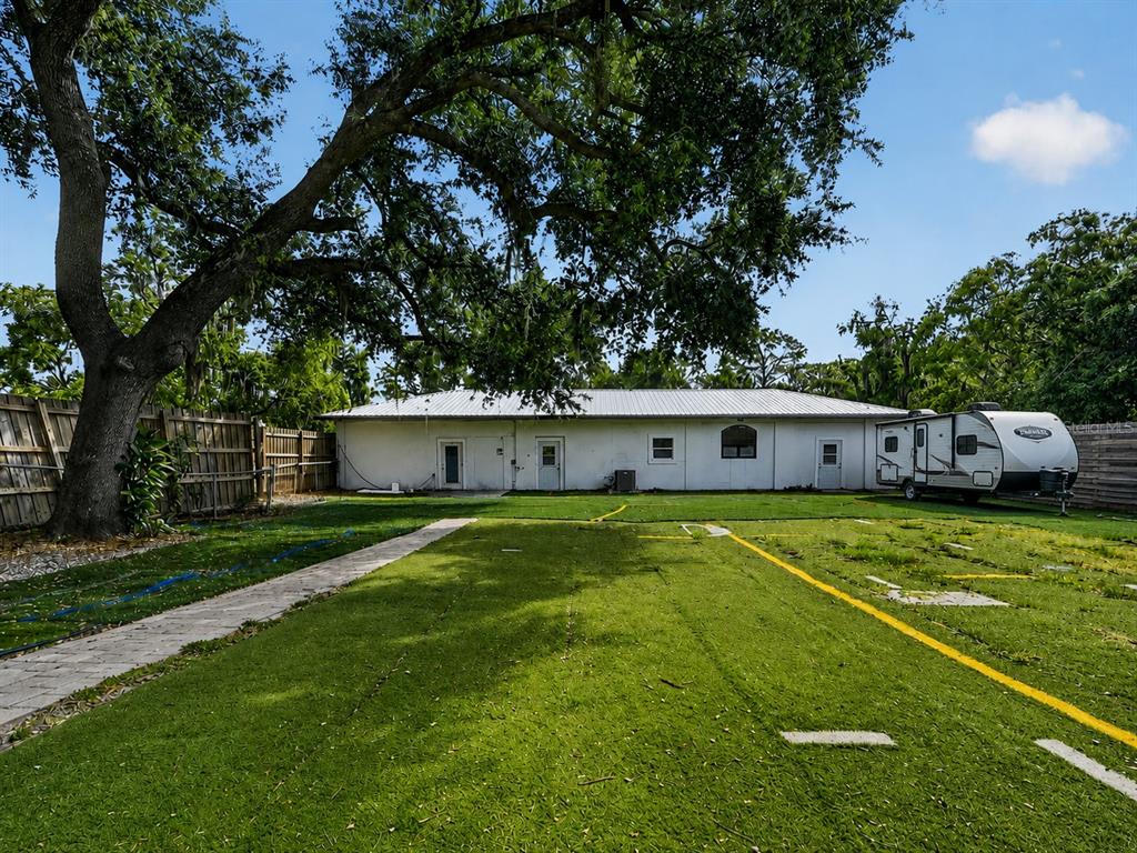 A grassy backyard features a white building, a large tree, and a parked travel trailer — 7311 PROCTOR ROAD, SARASOTA, FL