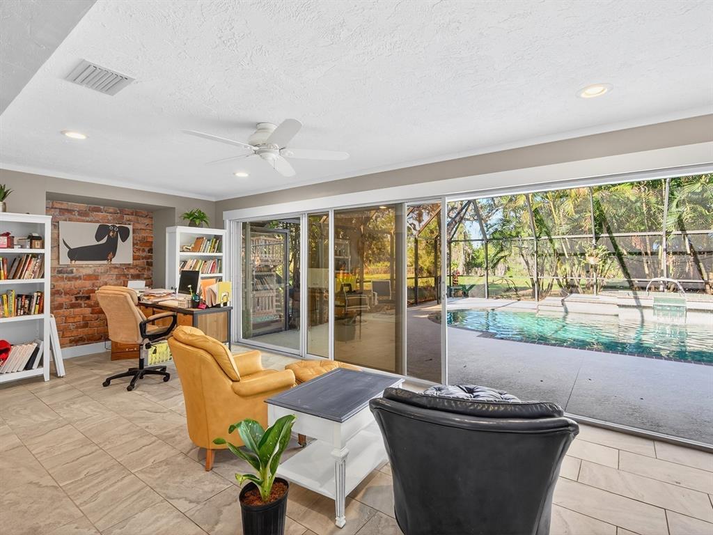 A home office with a brick wall, bookshelves, and sliding doors opening to a pool — 7311 PROCTOR ROAD, SARASOTA, FL