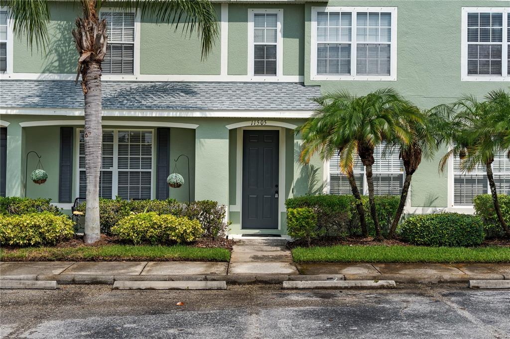 The exterior of a green two-story townhouse features a dark front door and palm trees — 11505 DECLARATION DRIVE, TAMPA, FL