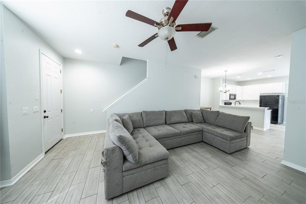 A living room features a large gray sectional sofa, tile flooring, and an open kitchen — 11505 DECLARATION DRIVE, TAMPA, FL