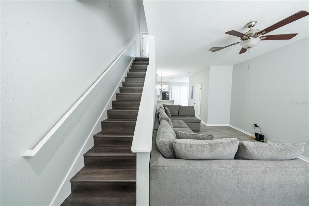 A staircase with dark wood treads sits beside a gray sectional sofa in a living room — 11505 DECLARATION DRIVE, TAMPA, FL