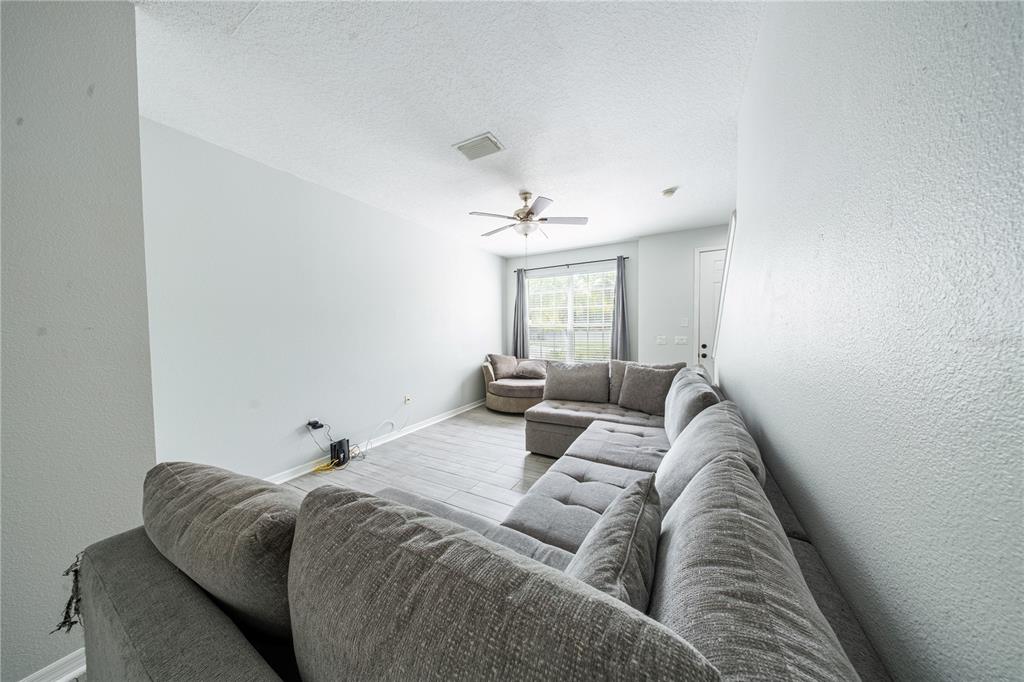 A living room features light gray walls, wood-look tile flooring, and a large sectional sofa — 11505 DECLARATION DRIVE, TAMPA, FL