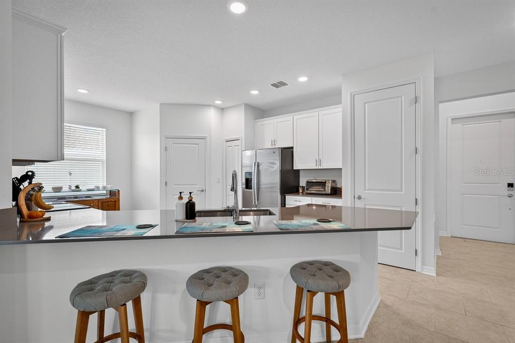 A kitchen features white cabinets, a gray island countertop, and three bar stools — 2607 HOPTREE LANE, EDGEWATER, FL