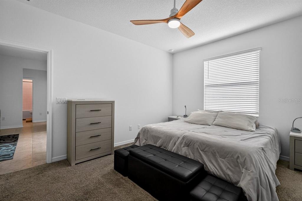 A bedroom features a bed with a black bench, a dresser, and a ceiling fan — 2607 HOPTREE LANE, EDGEWATER, FL