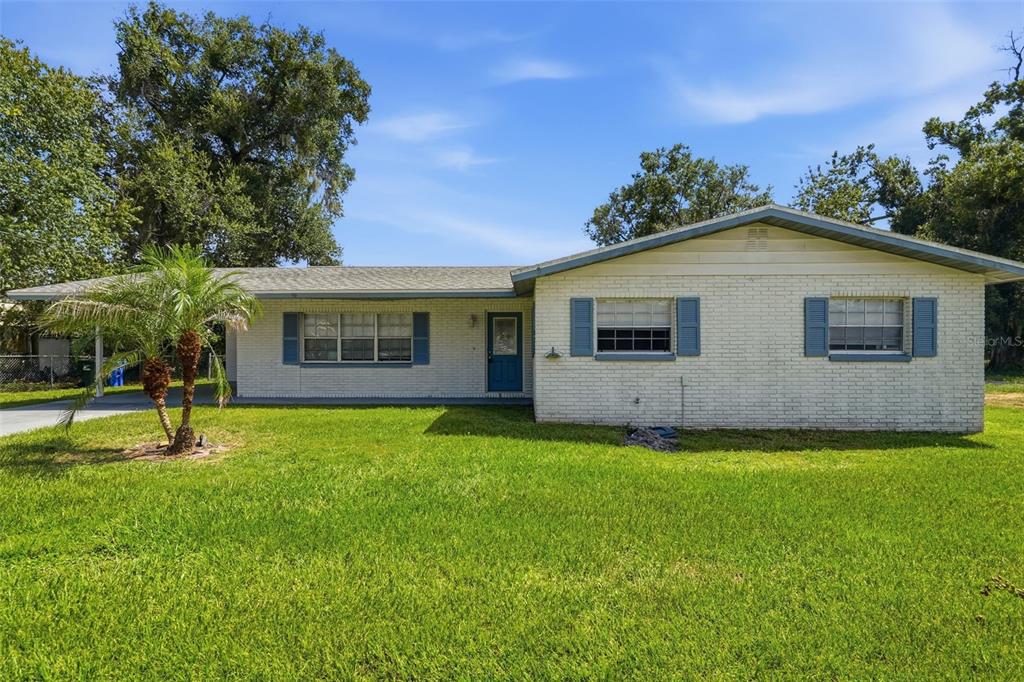 A single-story white brick house with blue shutters, a front lawn, and a carport — 1704 WAYMAN STREET, LAKELAND, FL