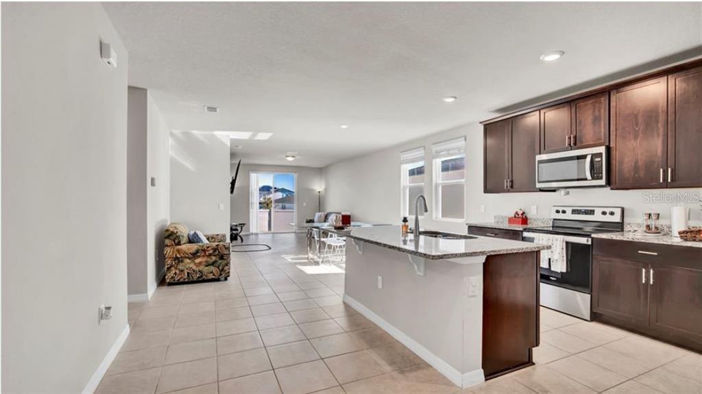 A kitchen with dark wood cabinets and a granite island overlooks an open living area — 3041 CASSIDY LANE, HAINES CITY, FL
